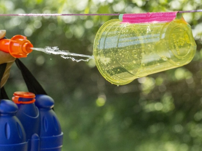 Child using squirt gun to spray plastic cup