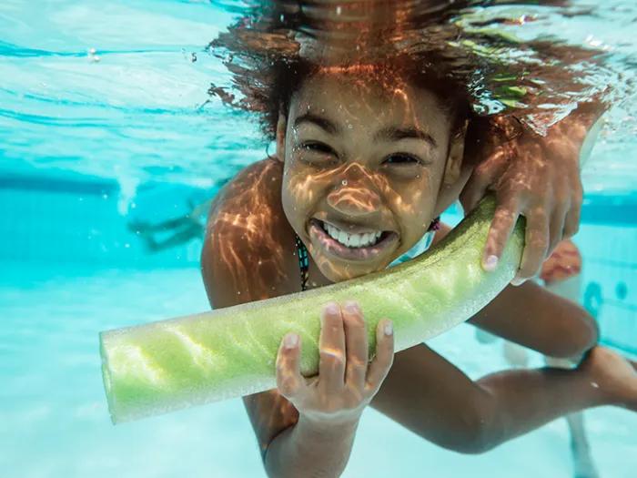 Child holding floaty and smiling underwater