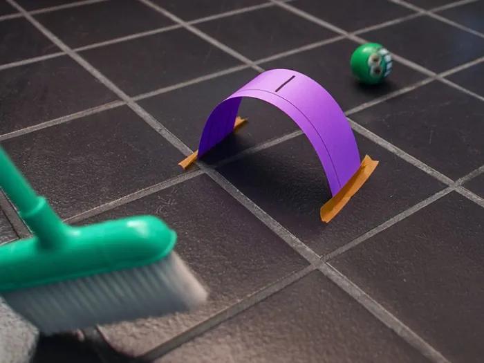 Person hitting ball with broom under homemade paper croquet strip