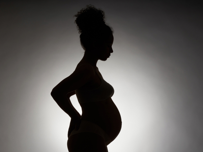 silhouette of pregnant woman black on grey background with white background behind the body glowing