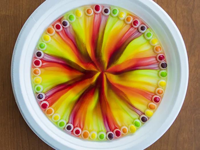 skittles circle a paper plate with water mixed in, forming a rainbow pinwheel
