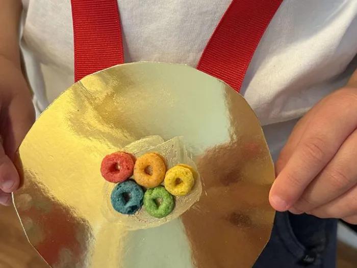 Olympics Gold Medal made out of gold paper plate, Colorful circle fruit cereal, and red ribbon.