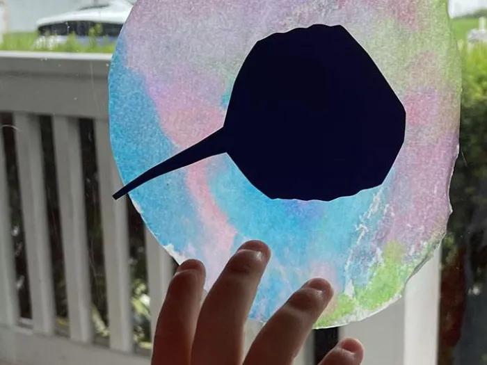 A tiny hand holds an ocean-themed suncatcher made out of paper and water color.