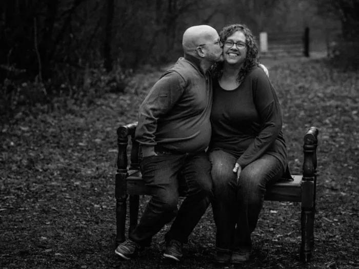 couple sitting on bench black and white kissing on cheek 
