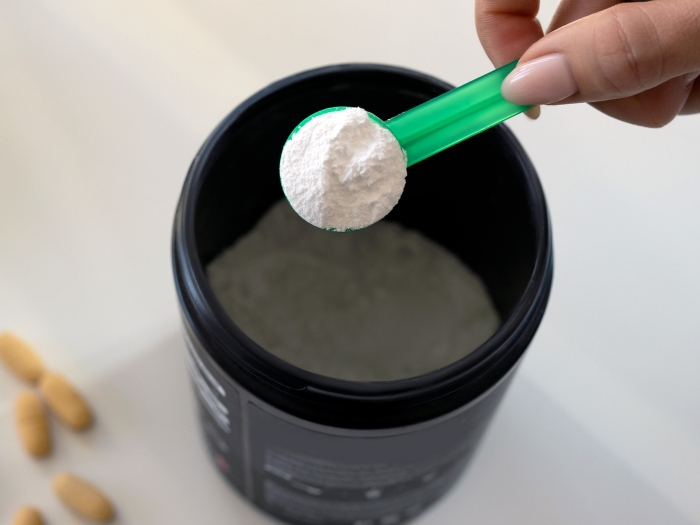 A hand holding a scoop of protein powder hovering over a cup of water