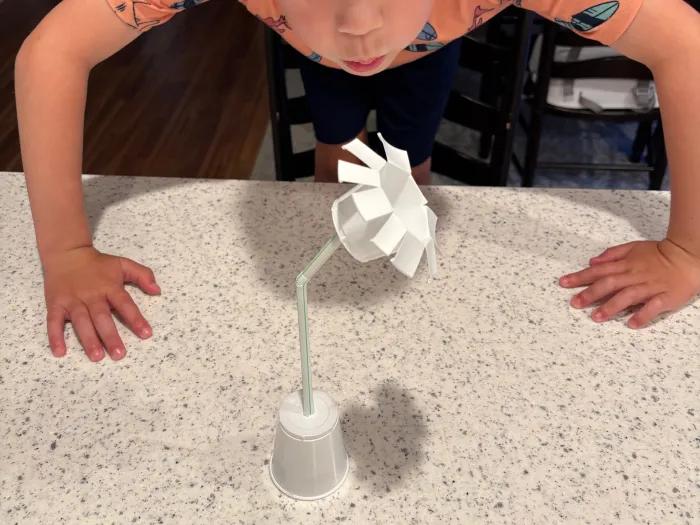 boy blowing on paper cup windmill to power it