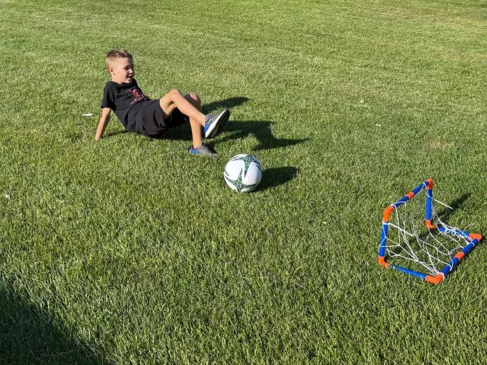 young boy in crab position kicking soccer ball with one leg