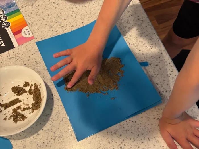 boy spreading sand onto blue sheet of paper
