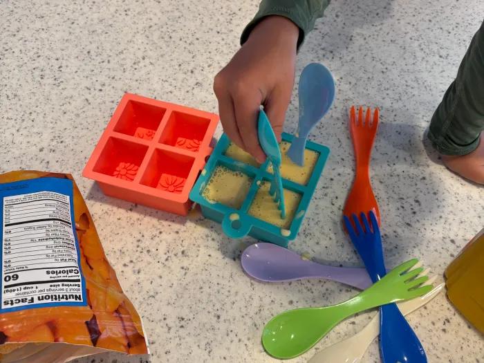 child placing plastic utensil into popsicle mold