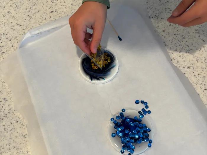 child placing sequins in glue circle