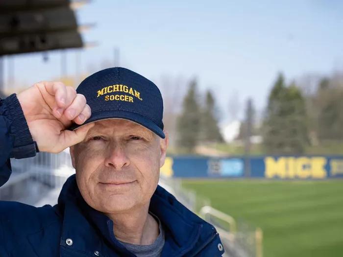 Steve Burns wearing his University of Michigan soccer hat while standing on the Michigan soccer field