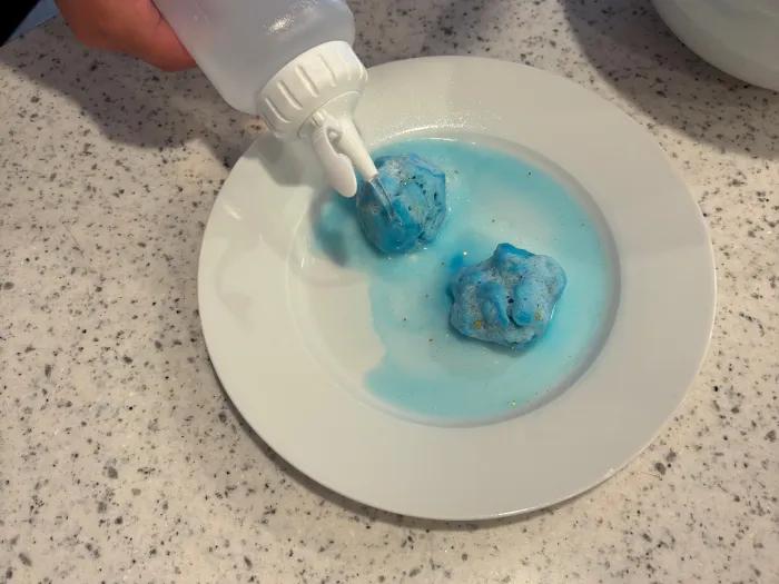 boy squeezing liquid from squeeze bottle over blue dough balls on plate