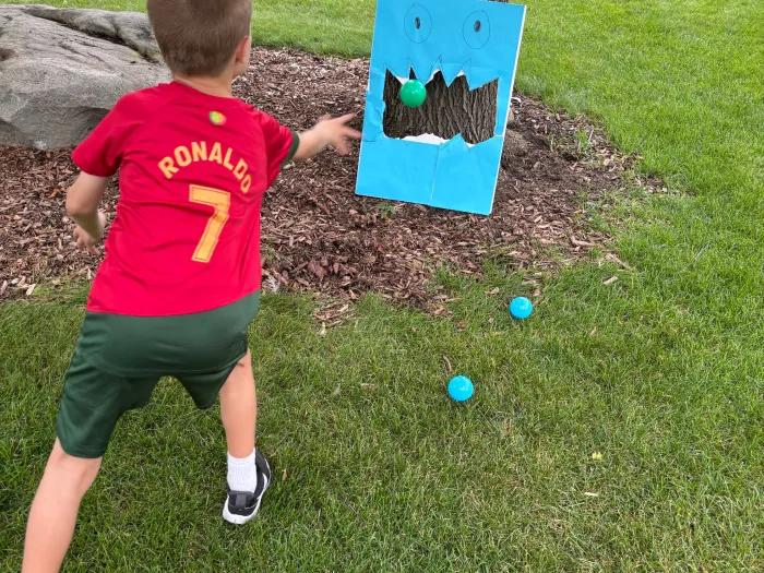 boy tossing ball into blue covered poster board with cutout in middle