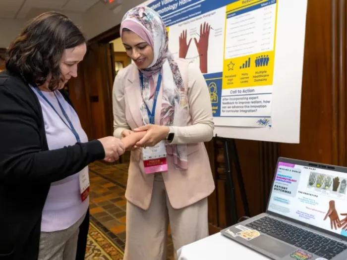 women looking at model hand in front of poster and computer on table next to them