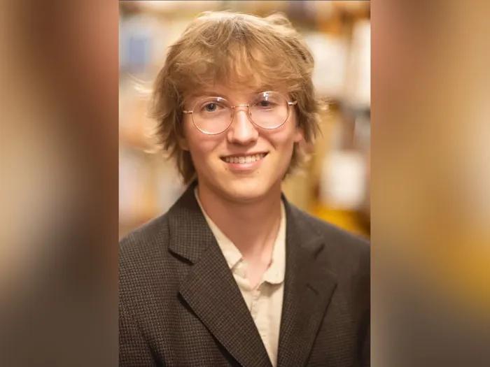 Portrait of Chase as a young adult. He is wearing glasses and a dark brown jacket over a button-down shirt.