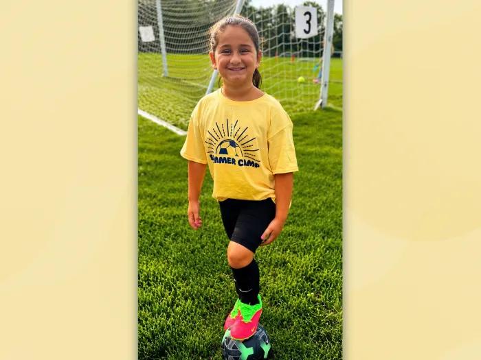 little girl with yellow shirt on soccer field smiling ready for soccer