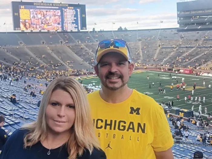 Double portrait of Jennifer Strohpaul and her fiancé standing together with the Big House visible behind them.