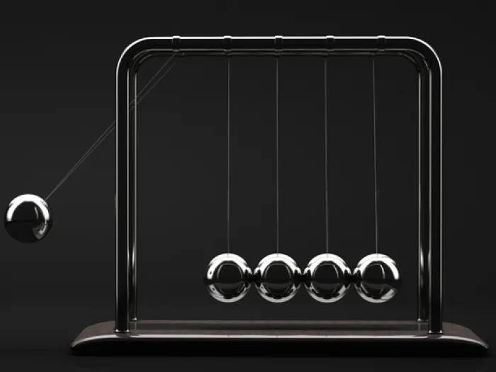 Newton’s cradle with one metal ball raised and four balls resting together against a black background.