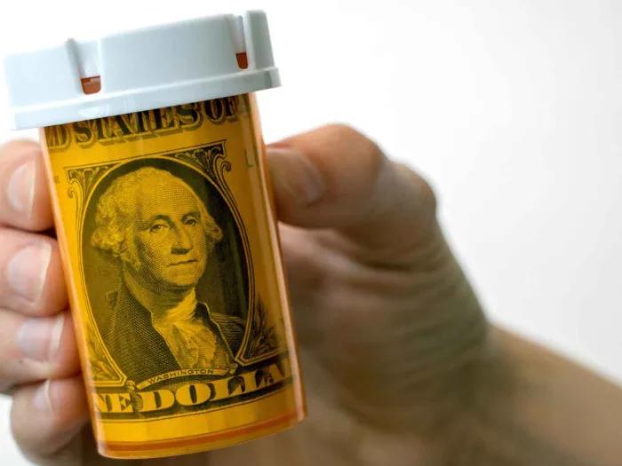 A hand holding a prescription bottle with a dollar bill in it
