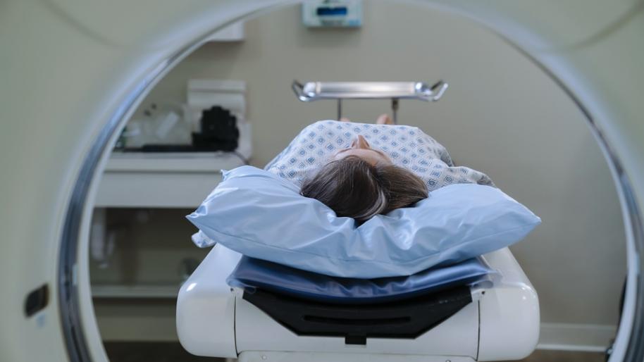 Female in hospital gown lying on gurney waiting at mouth of imaging machine