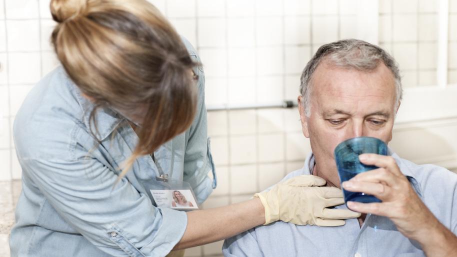 Healthcare worker checking man's throat as he drinks. 