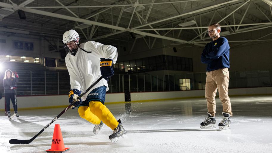 Man wearing blue shirt watching a player practicing hockey.