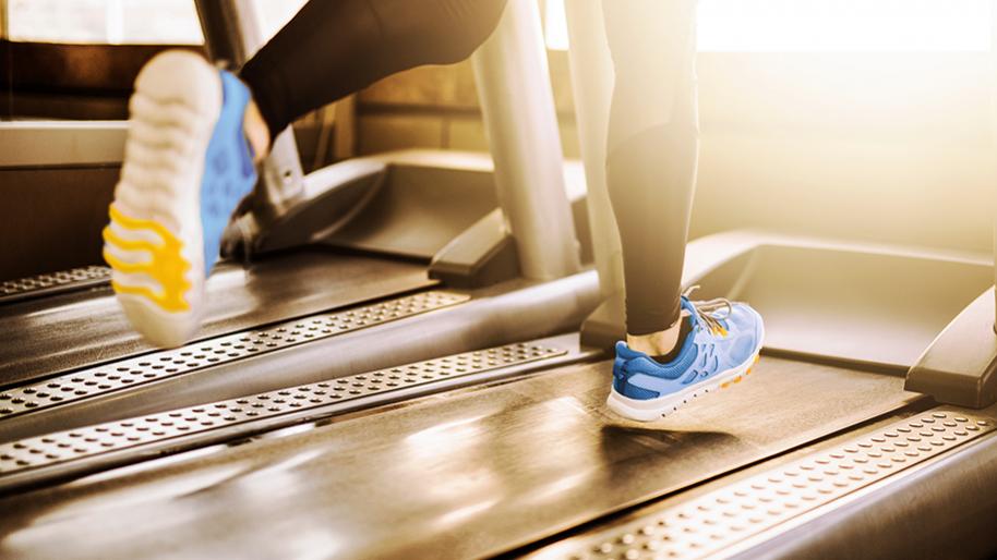 Legs of person wearing black tights and blue running shoes running on a treadmill