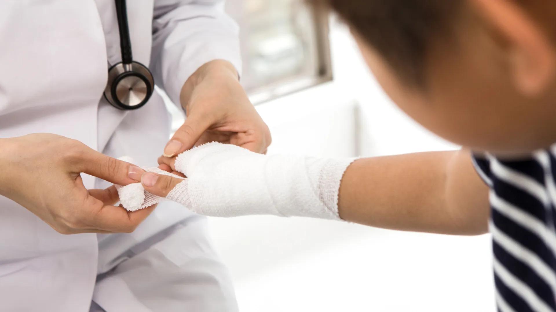 Young child with gauze wrap on their wrist & hand being examined by a physician