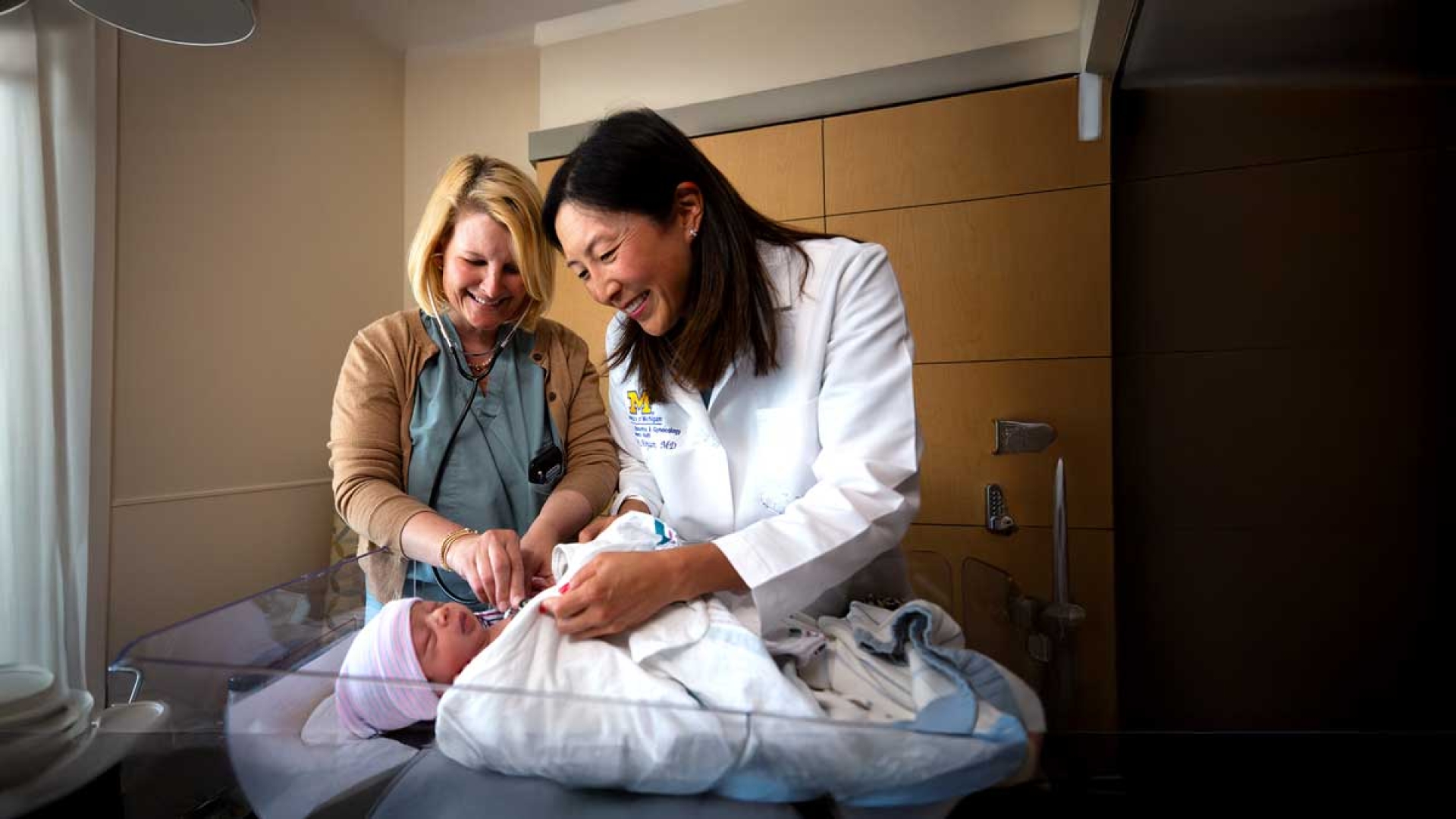 A doctor and nurse smiles as they swaddle a newborn baby