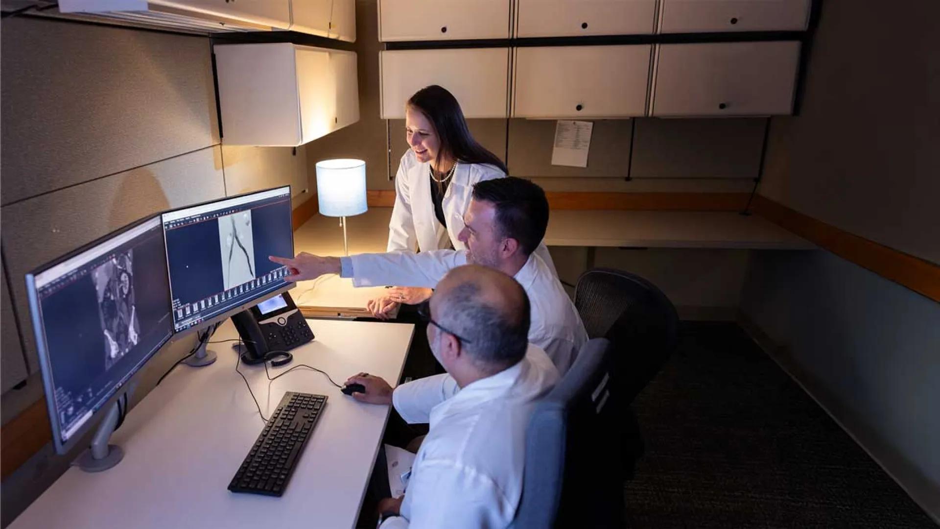 Three doctors review patient's imaging on two computer monitors