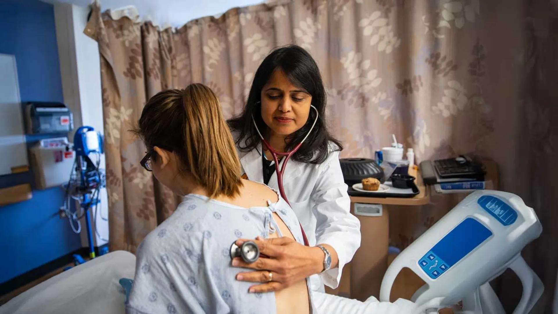 A doctor examines a patient from her hospital bed. 