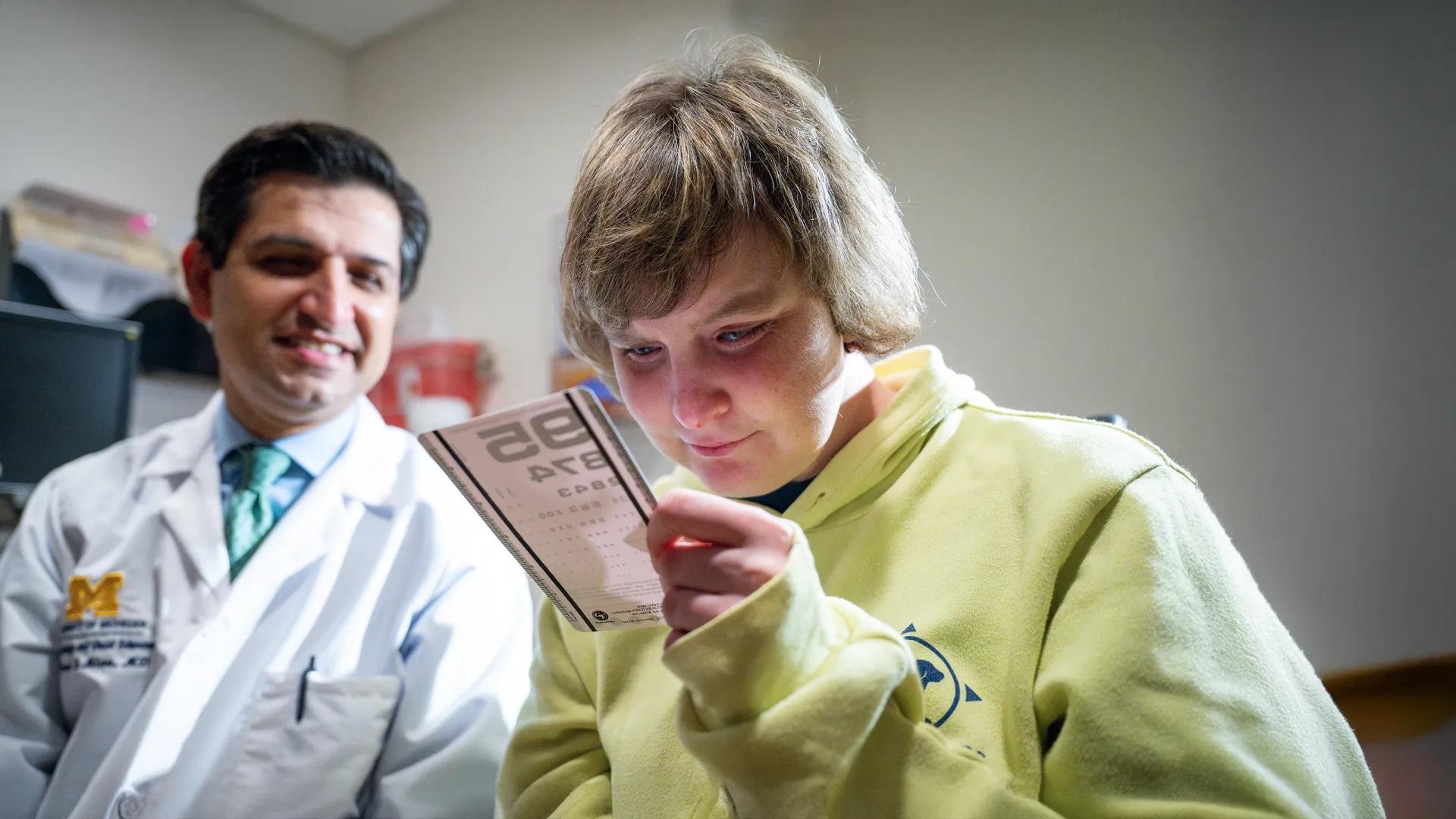 Dr. Shahzad Mian with a patient in a bright green sweatshirt holding a visual acuity card.