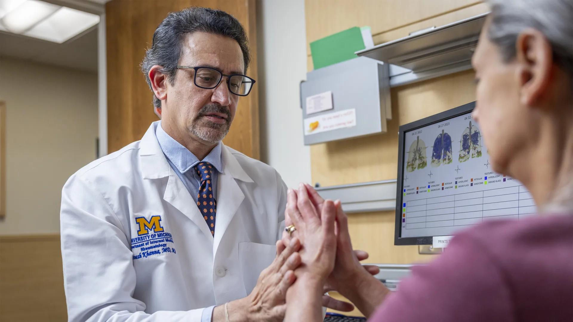 Male U-M Health doctor with glasses examining hands of female patient