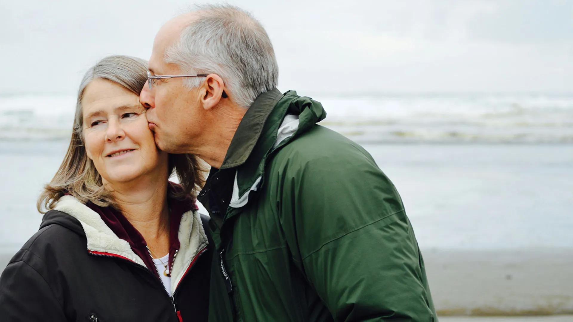 Older man kisses an older woman on a beach