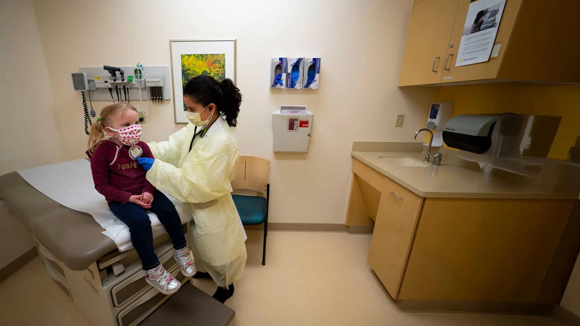 A doctor examines a little girl who is sitting on an examination table.