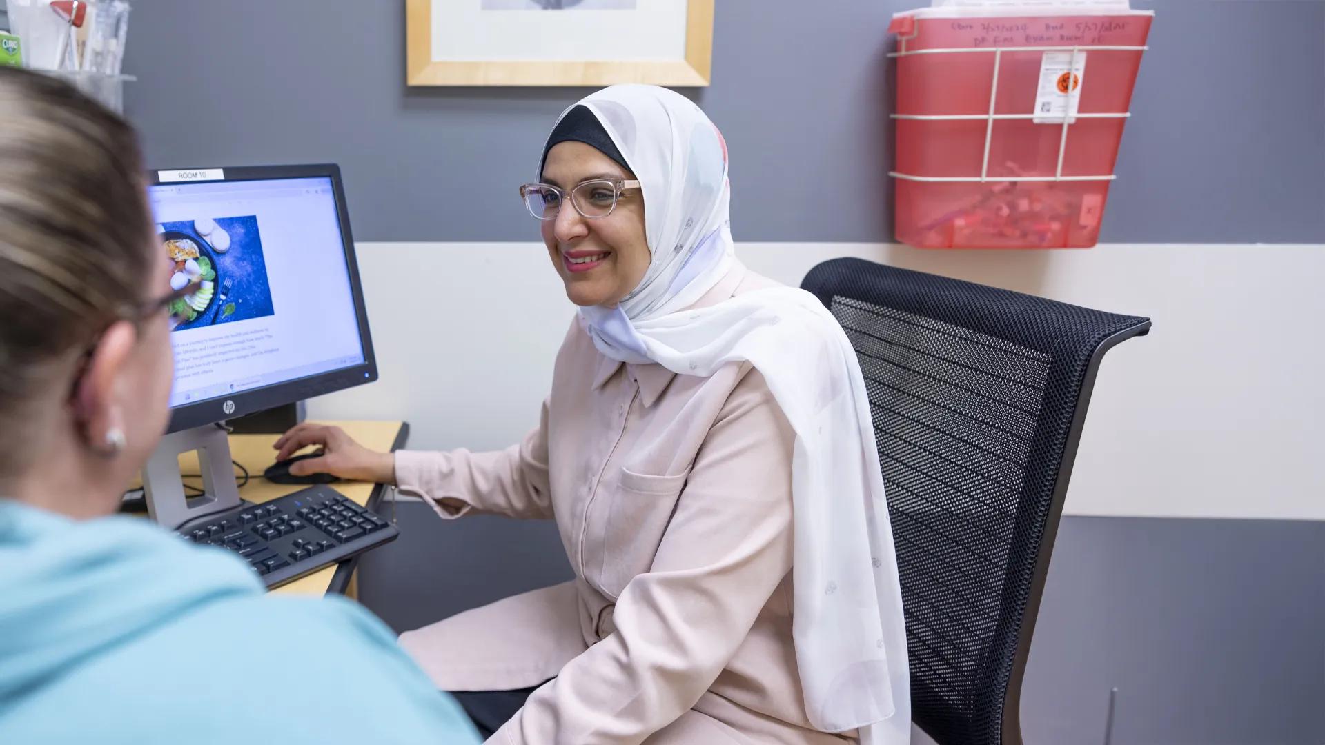 Care provider wearing glasses and head covering smiling at female patient shown from the back