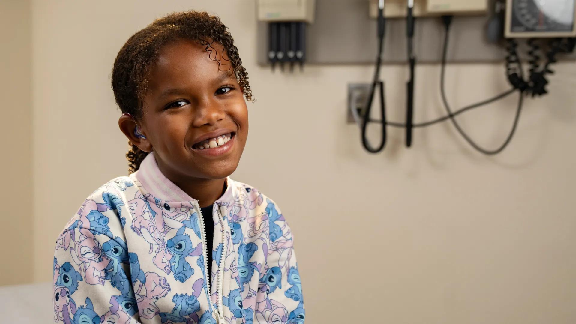 Black girl with flowered jacket smiling with medical equipment in background