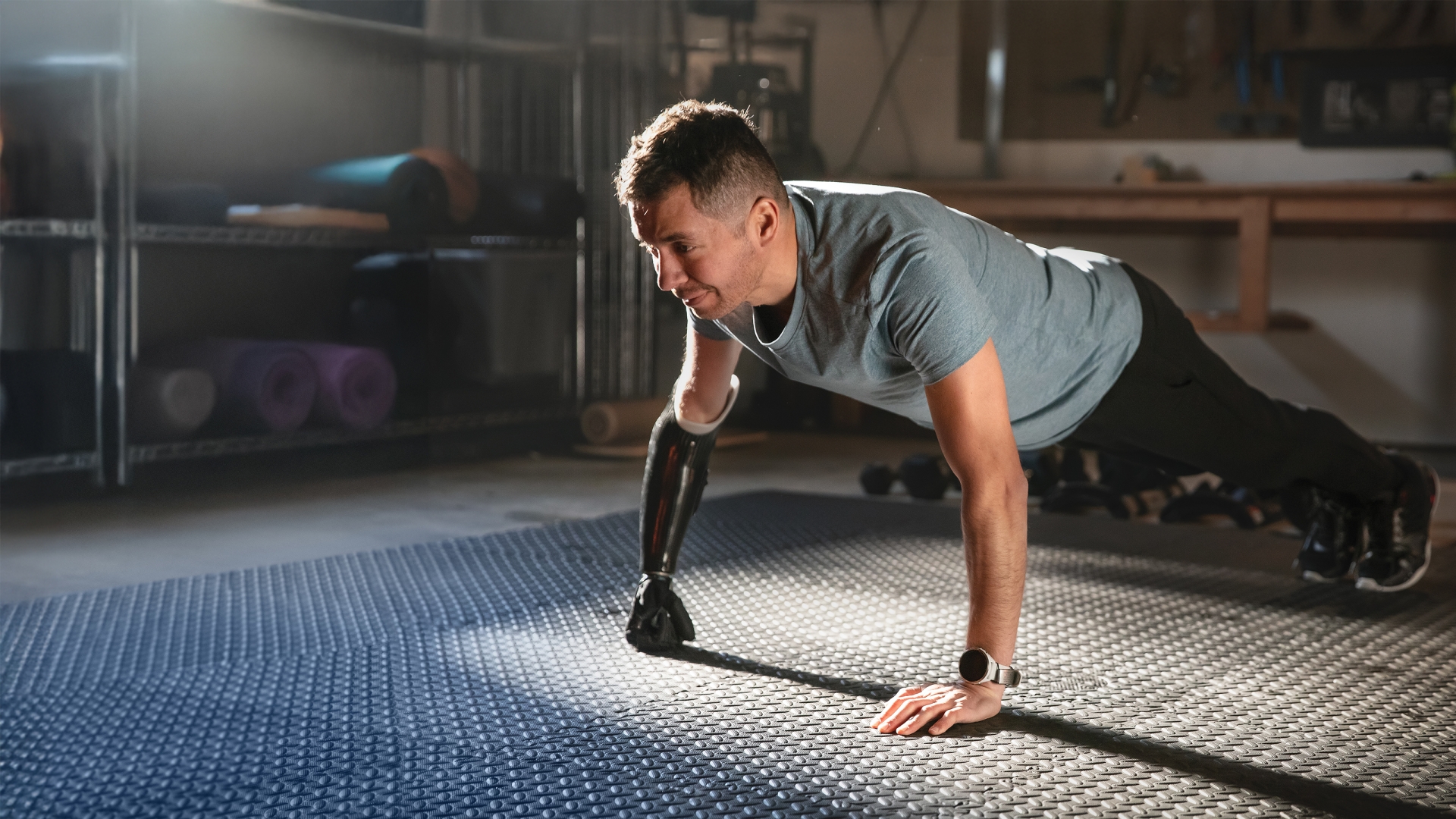 Man with prosthetic arm holding a plank pose with sun streaming into room