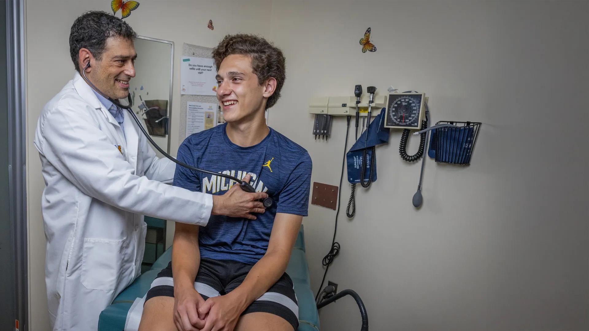 Male doctor holding a stethoscope on teenage boy patient wearing blue tshirt