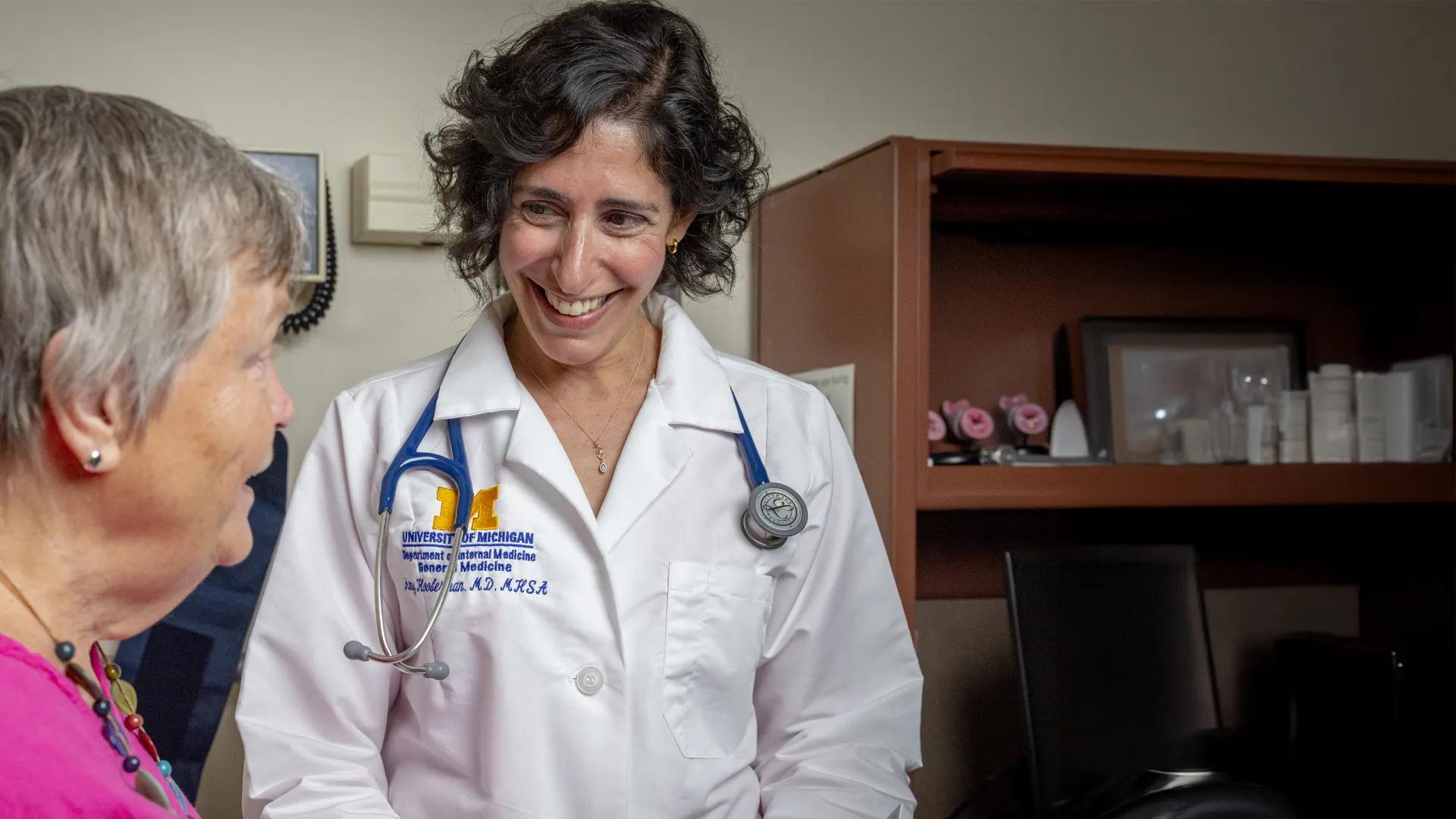 Smiling female doctor with short dark hair talking with older woman wearing a bright pink shirt