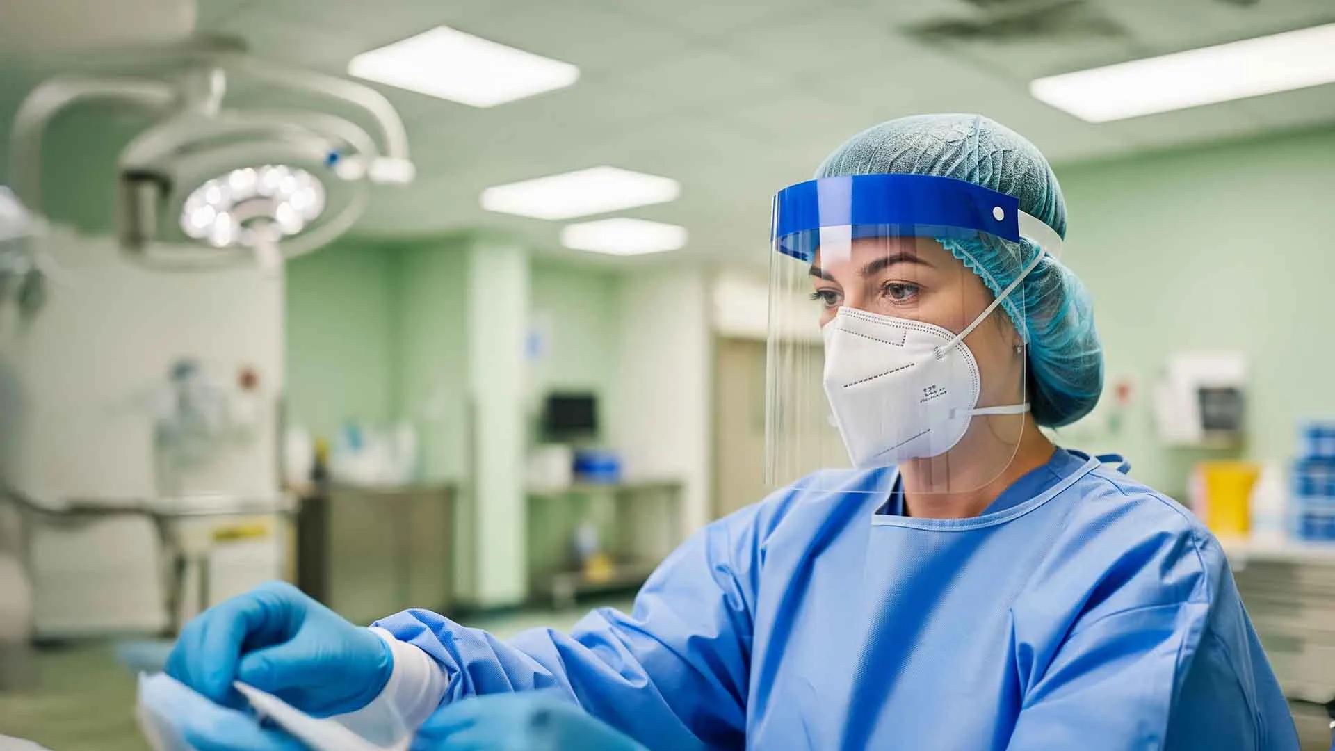 A woman works in a lab. She wears a face mask and shield.