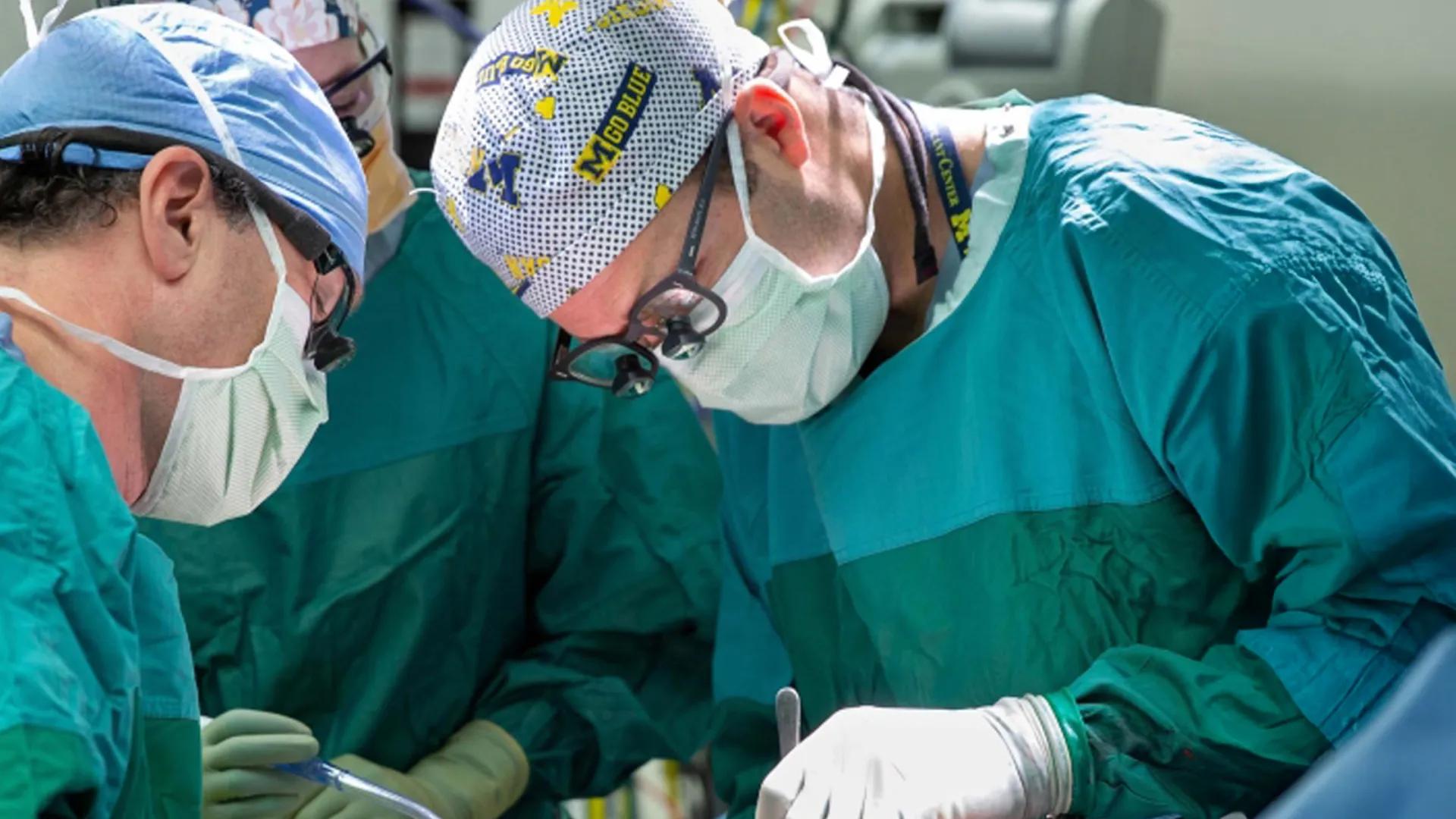 Surgeons operating with one wearing "M Go Blue" branded surgical cap