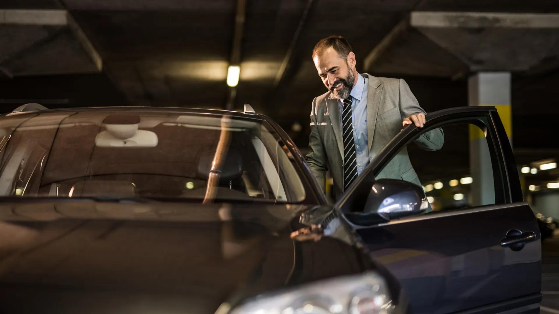 Man wearing suit opening the door of his car smiling.