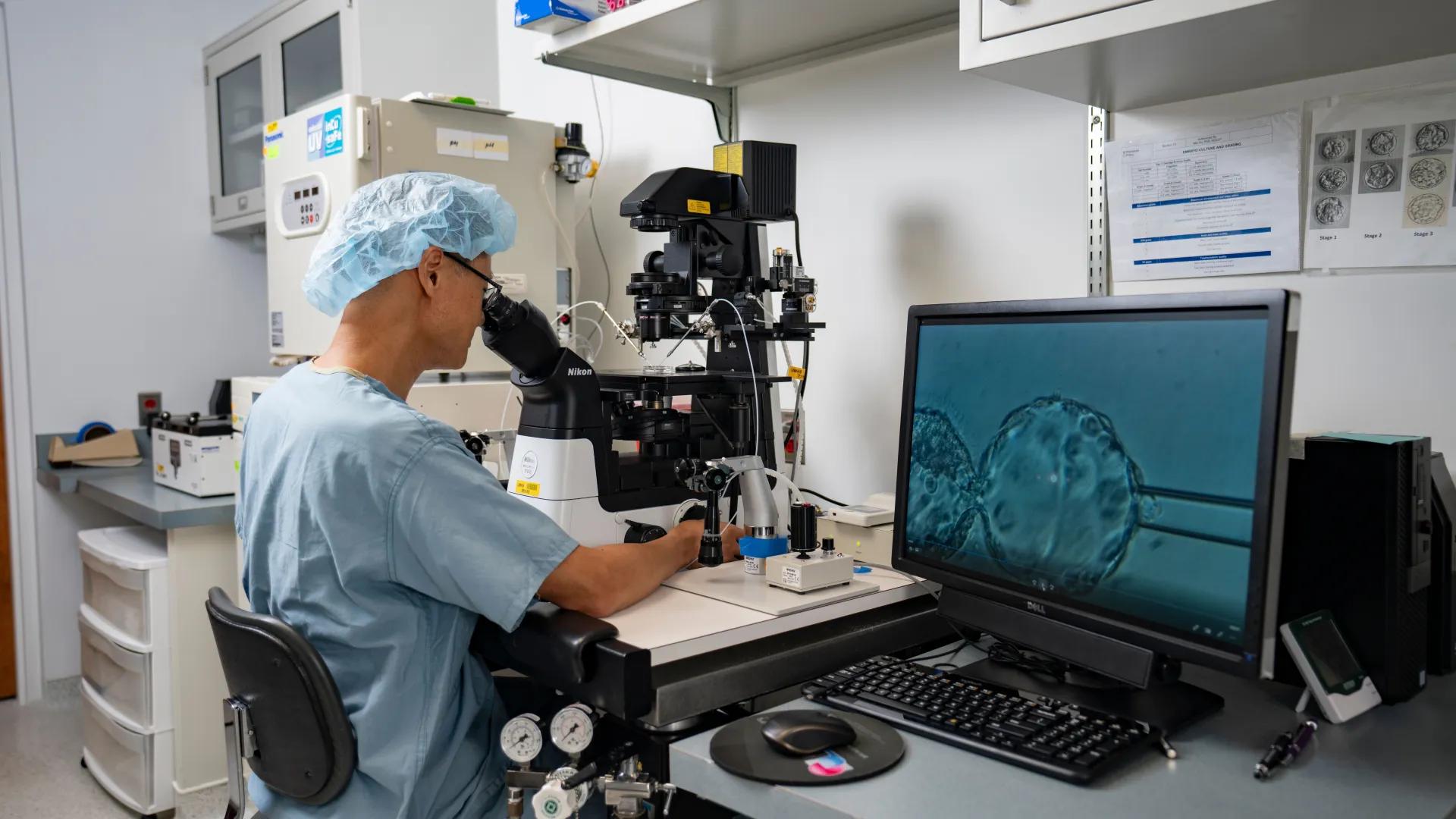 A health care professional examining through a microscope in lab.