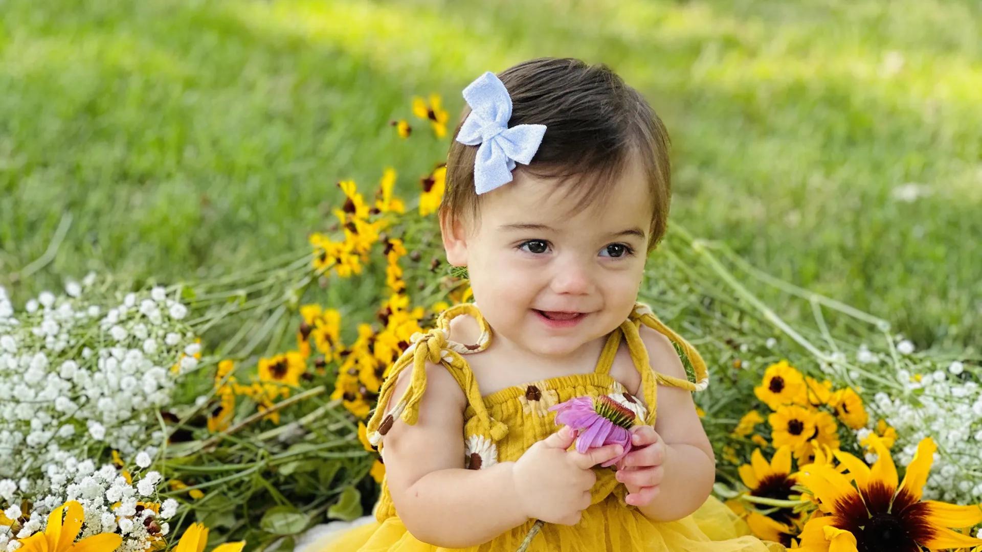 Child in a yellow dress with a white bow in their hair sitting in the grass surround by daisies and baby's breath 