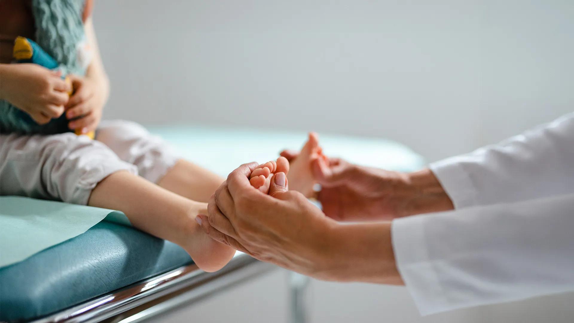 A child sits on an examination table while a doctor examines their feet.