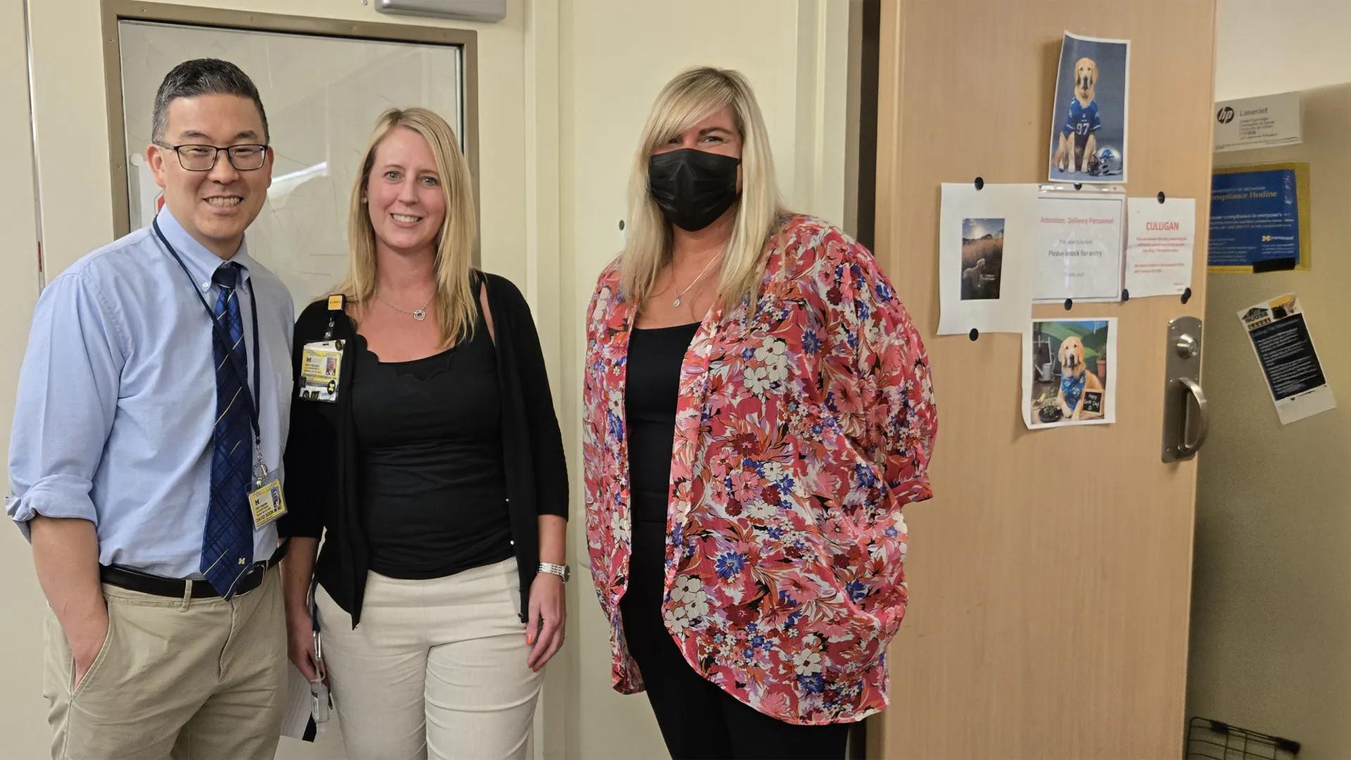 One Asian man and two blond women smiling, one wearing a face mask
