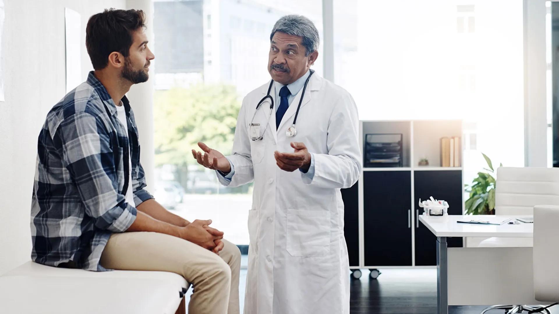 Adult bearded man speaks to an older male doctor