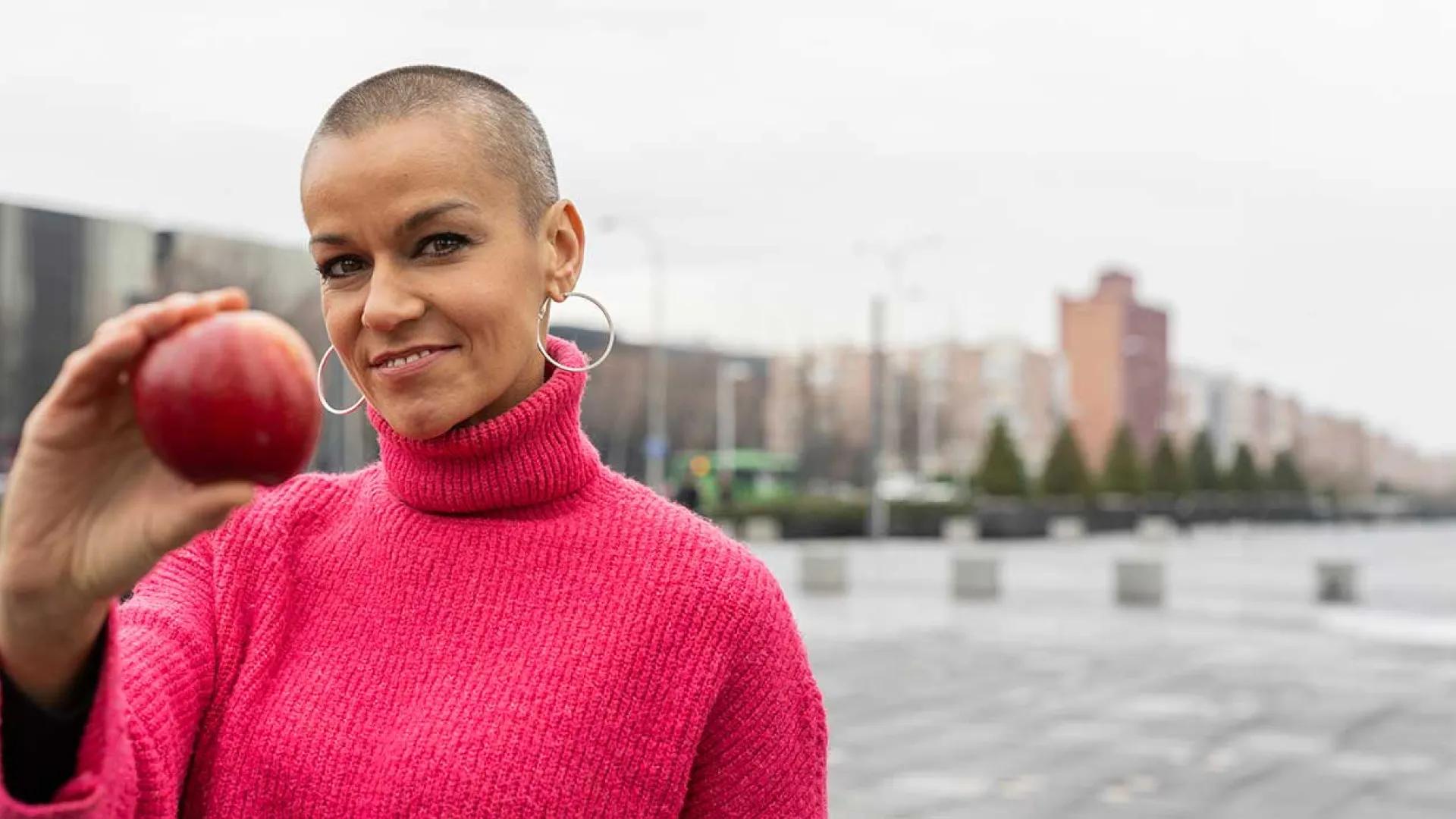 Mixed race woman holds an apple and wears a pink sweater
