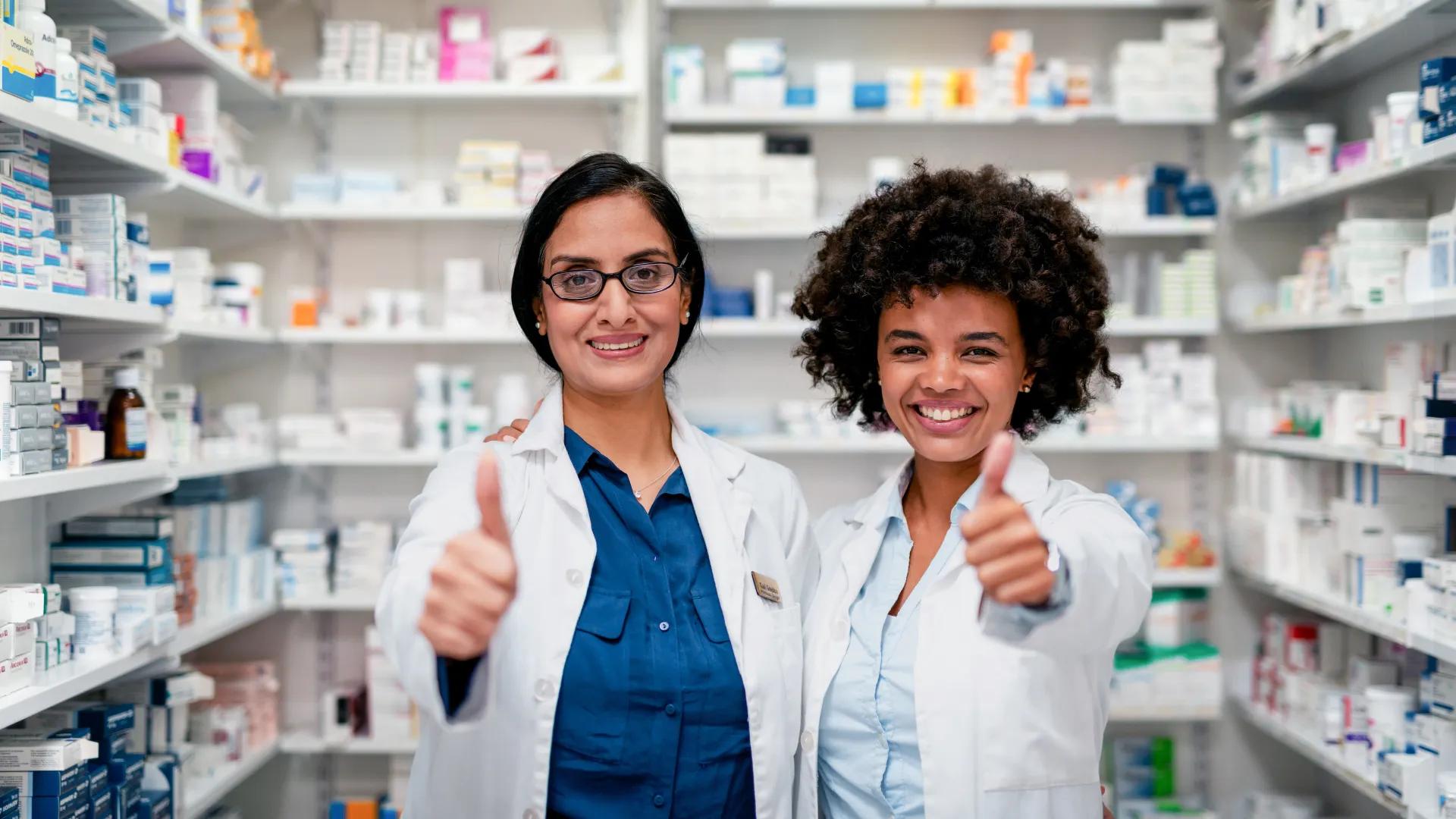 Two Professional Pharmacists Smiling and Giving Thumbs Up in a Pharmacy Setting.